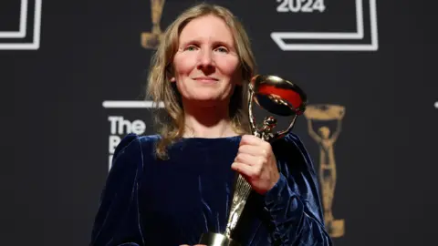 EPA Samantha Harvey holding the Booker Prize trophy at the 2024 ceremony