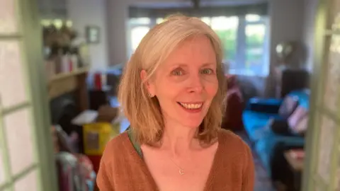 Piers Hopkirk/BBC A picture of Elaine Hills in her house. Elaine is wearing a burnt orange cardigan. 