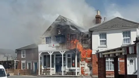 Essex County Fire and Rescue Service A building on fire. You can see the fire coming out of the building and smoke coming out towards the fire 