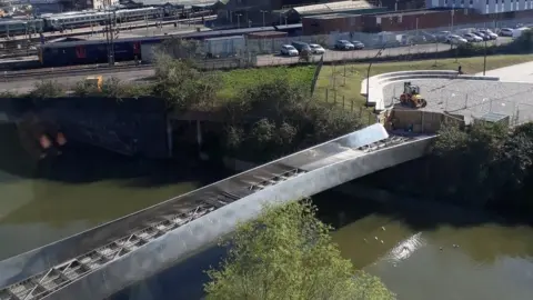 Avison Young Property Management Consultancy An aerial image showing the metal bridge over a brown-green river. The deck panels have been lifted during resurfacing work. In the background you can see trains on the track at Temple Meads Station. 