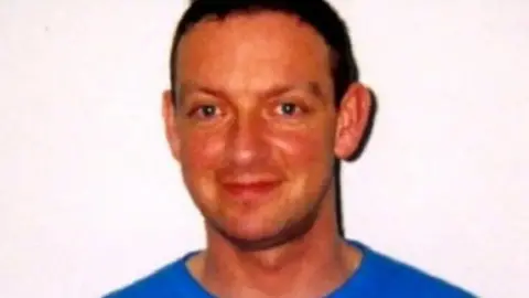 BBC Colin Norris smiling at the camera wearing a blue top, with dark brown hair and stood in front of a white background 